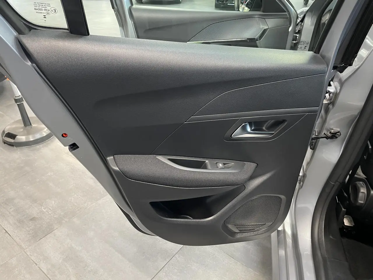 Vue intérieure de la porte arrière droite gris clair de la Peugeot 208 2024 avec commande de vitre et haut-parleur intégré.