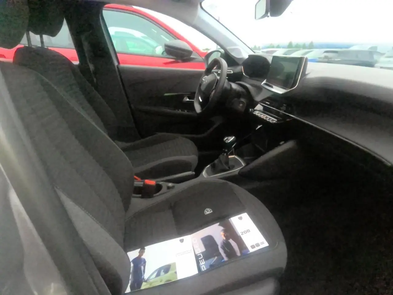 Vue intérieure côté conducteur de la Peugeot 208 gris clair, avec sièges tissu et écran tactile central visible.
