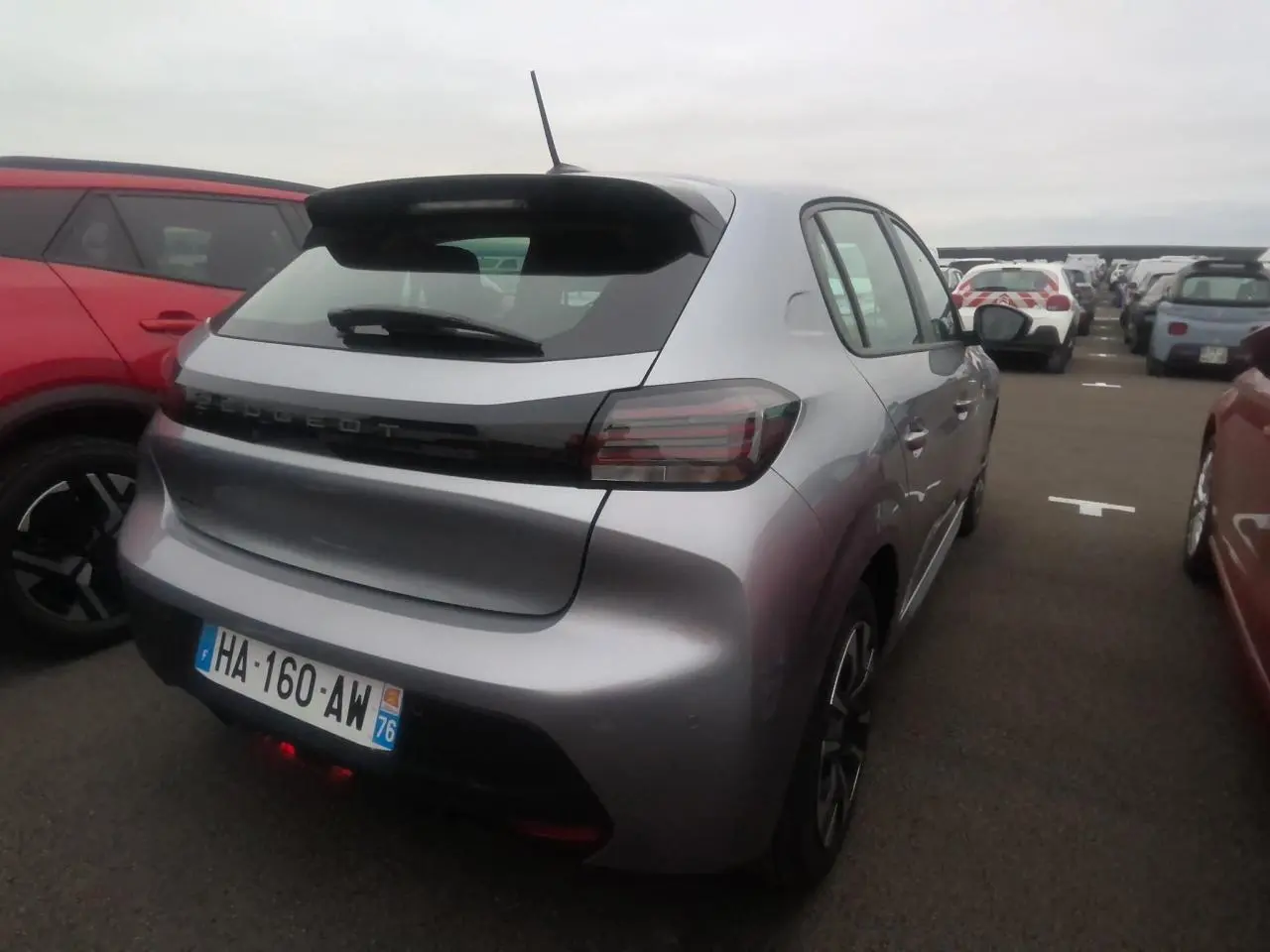 Vue 3/4 arrière droite d'une Peugeot 208 gris clair avec becquet noir brillant et feux arrière à LED signature 3 griffes.