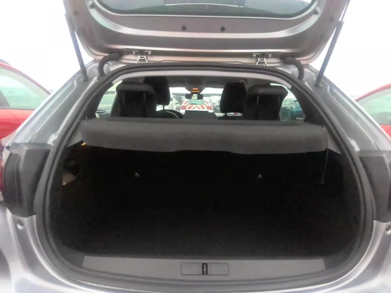 Coffre ouvert vu de l'arrière d'une Peugeot 208 gris clair, montrant l'espace de chargement et l'intérieur sombre.