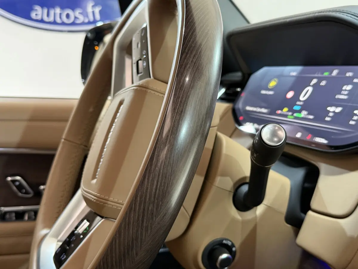 Gros plan sur le volant bois et cuir beige du Range Rover PHEV 2024 avec tableau de bord digital et levier de vitesses.