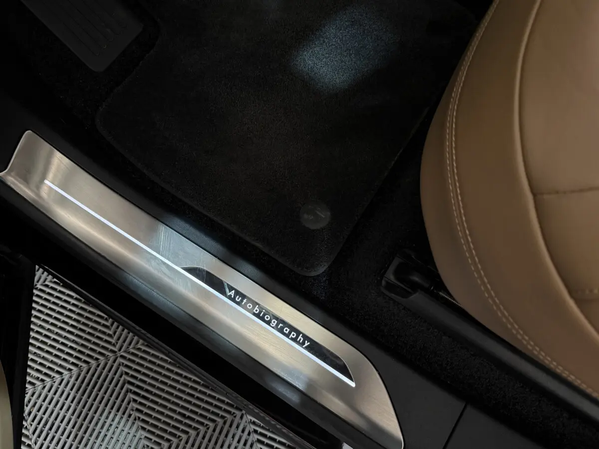 Détail intérieur montrant la plaque de seuil de porte "Autobiography" sur un Range Rover noir avec siège cuir beige.
