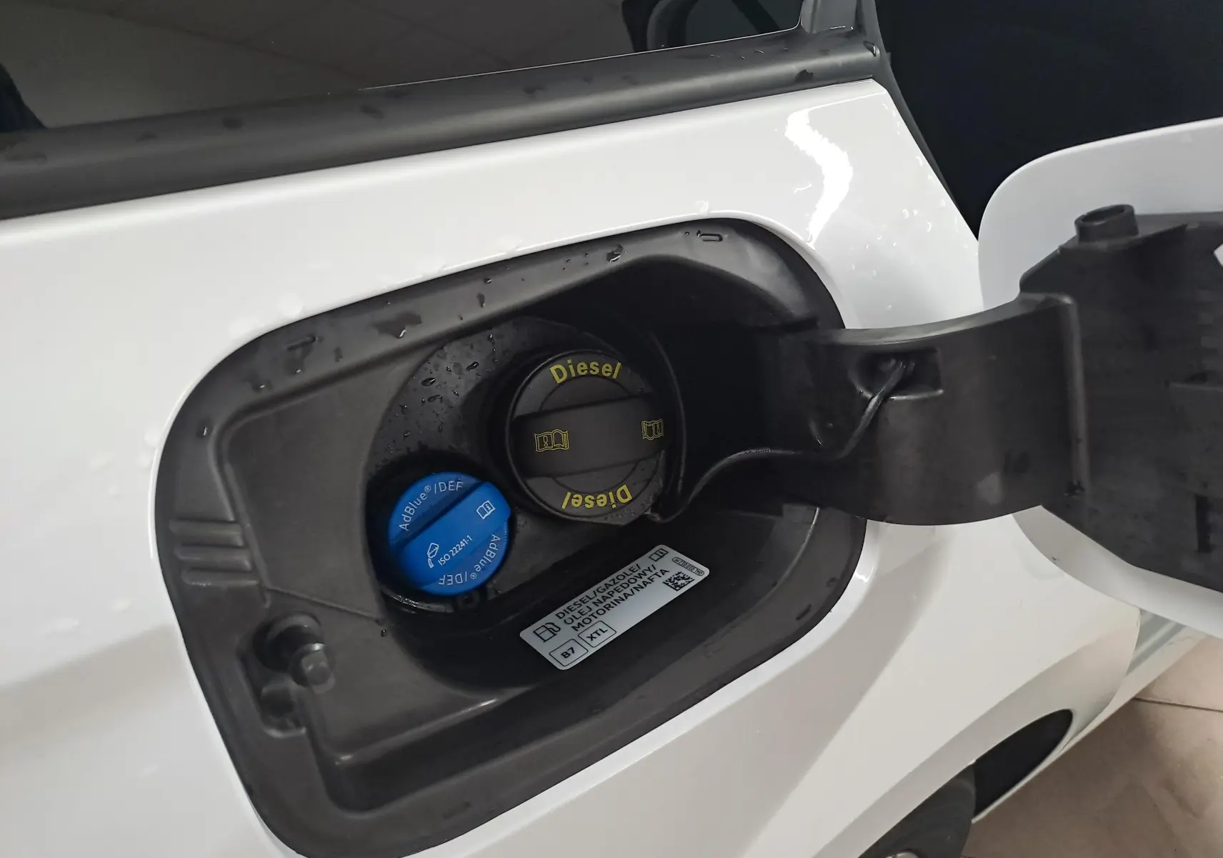 Gros plan sur la trappe à carburant ouverte d’une Skoda Octavia Combi blanc Moon, avec bouchons Diesel et AdBlue visibles.