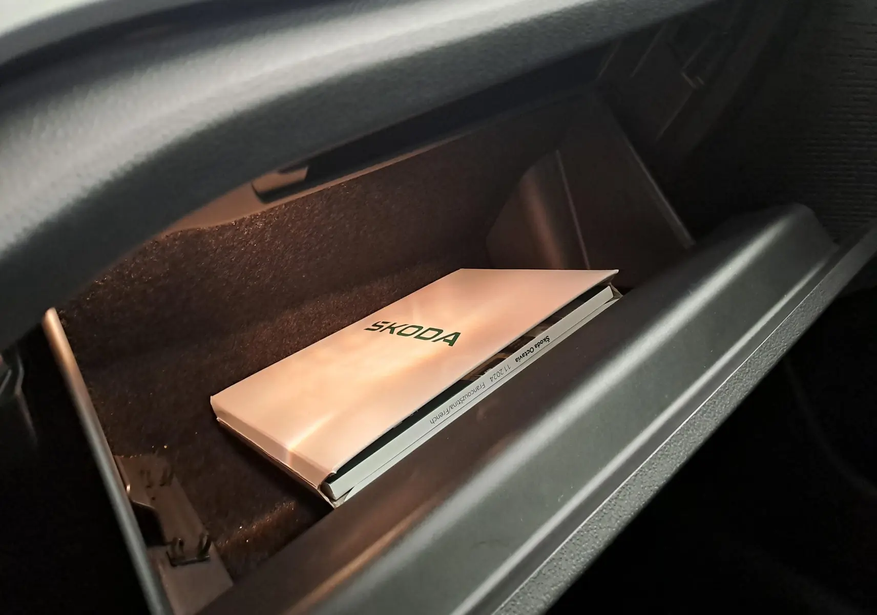 Gros plan sur la boîte à gants ouverte d’une Skoda Octavia Combi, avec un manuel Skoda visible à l’intérieur.