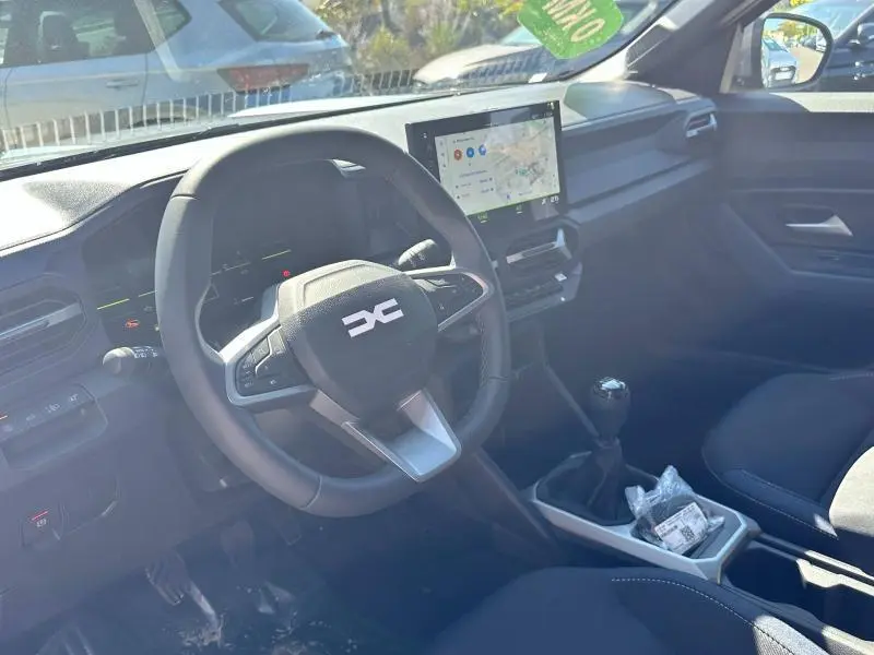 Vue intérieure côté conducteur du Dacia Bigster blanc 2025, volant multifonction, écran tactile et levier de vitesses manuel visibles.