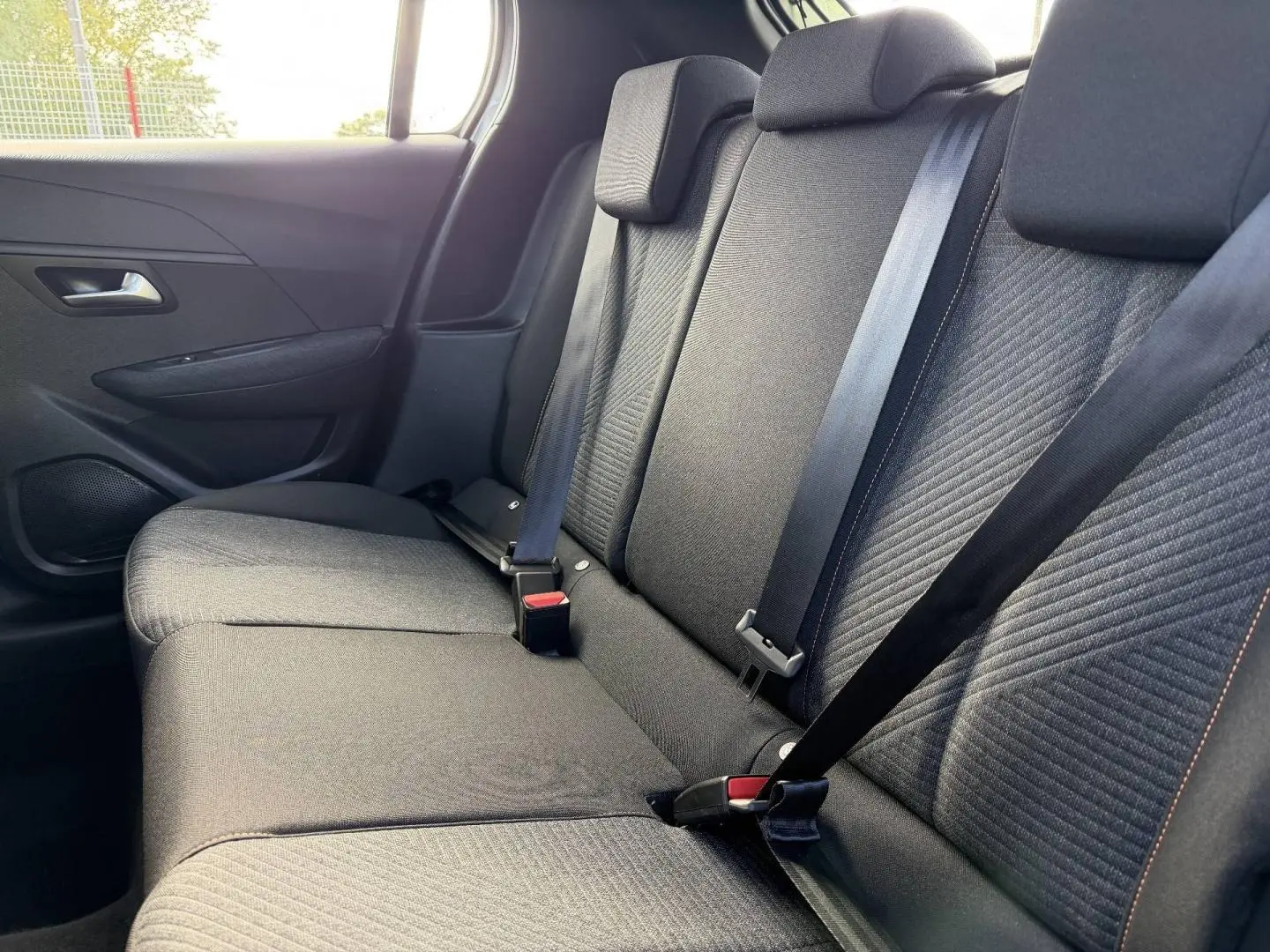 Vue intérieure côté droit sur la banquette arrière en tissu gris avec surpiqûres orange de la Peugeot 208 1.2 Hybrid 2025.