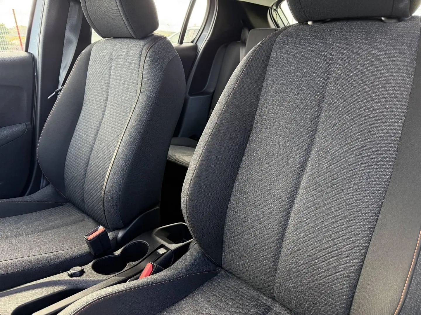 Gros plan sur les sièges avant en tissu gris avec surpiqûres orange de la Peugeot 208 1.2 Hybrid 110ch Style.