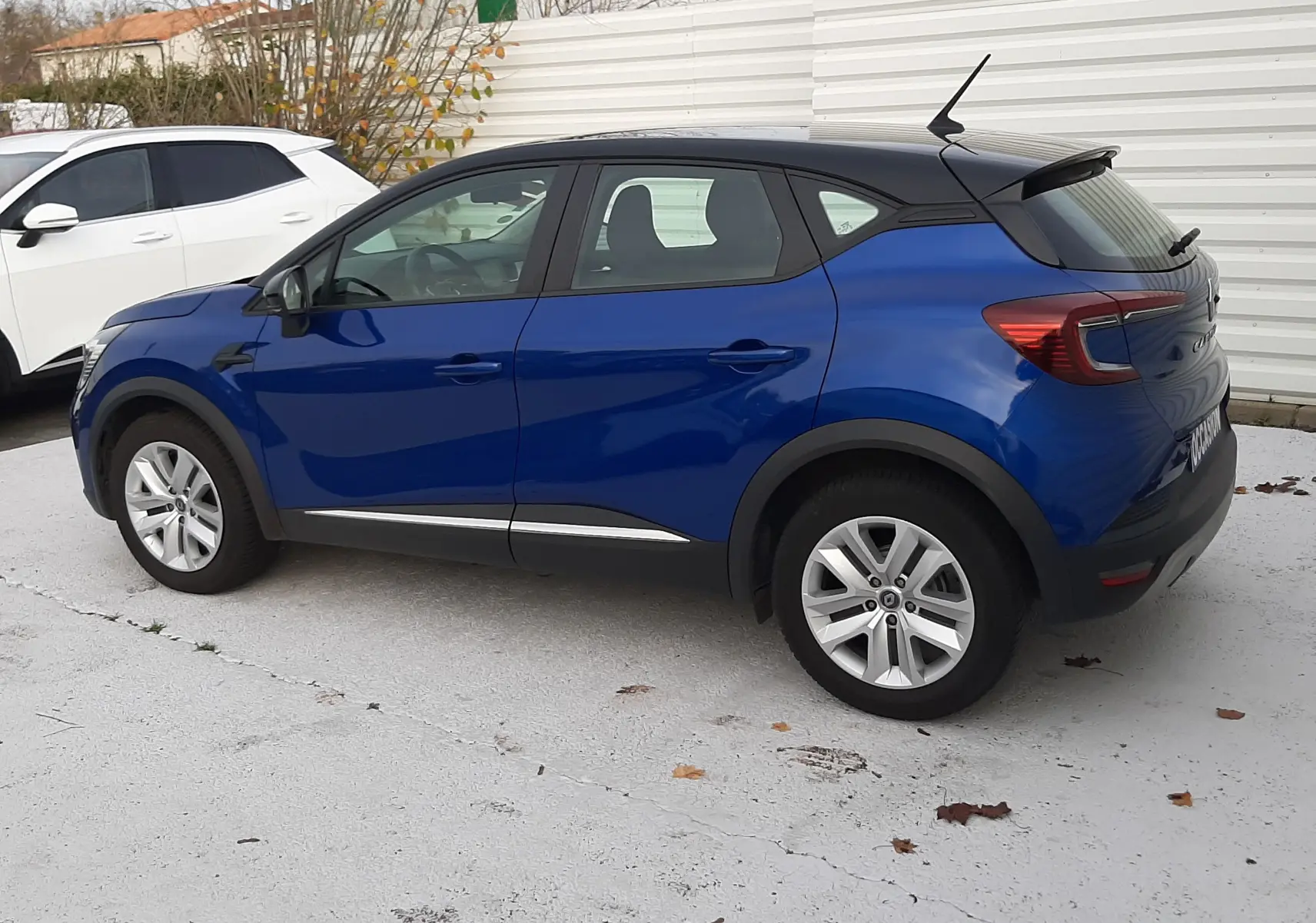 Renault Captur 1.5 Blue DCI 115ch Business bleu iron avec toit noir, vue de profil côté gauche sur parking.