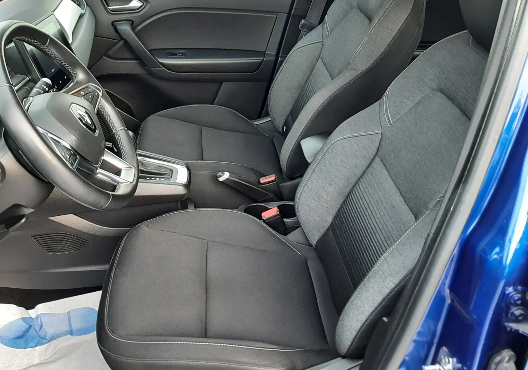 Intérieur avant gauche du Renault Captur bleu iron, sièges tissu noir et volant multifonction visible.