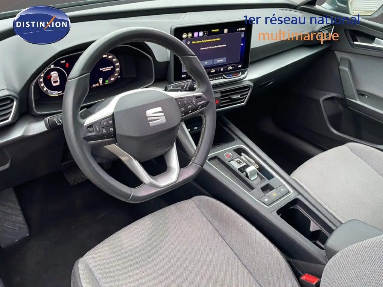 Intérieur SEAT Leon 2025 vu côté conducteur, volant multifonction, écran tactile central et sièges tissu gris clair.