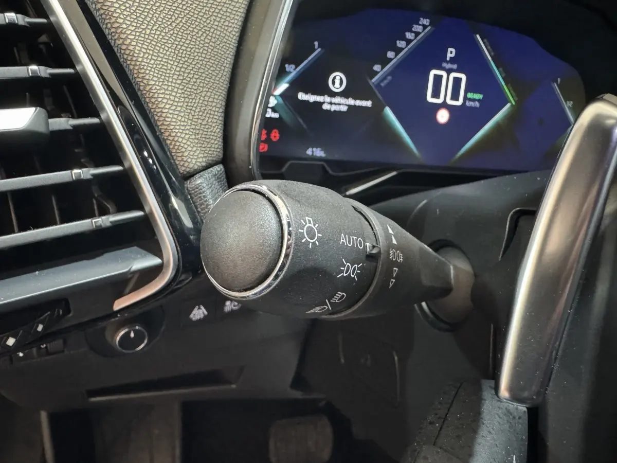 Gros plan sur la commande des phares à gauche du volant dans le tableau de bord numérique du DS7 Crossback gris foncé.
