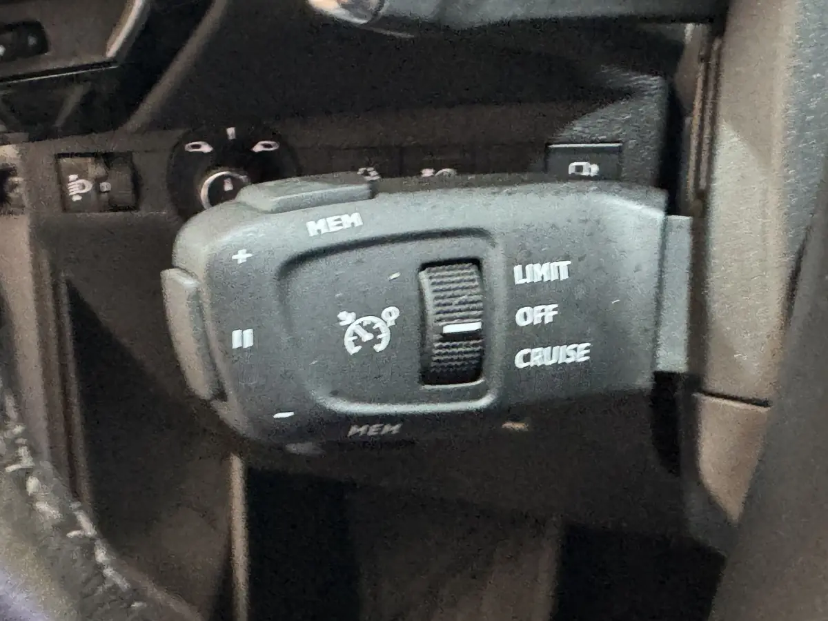 Gros plan sur la commande de régulateur de vitesse du DS7 Crossback E-TENSE 225 Bastille+ avec marquages blancs sur fond noir.