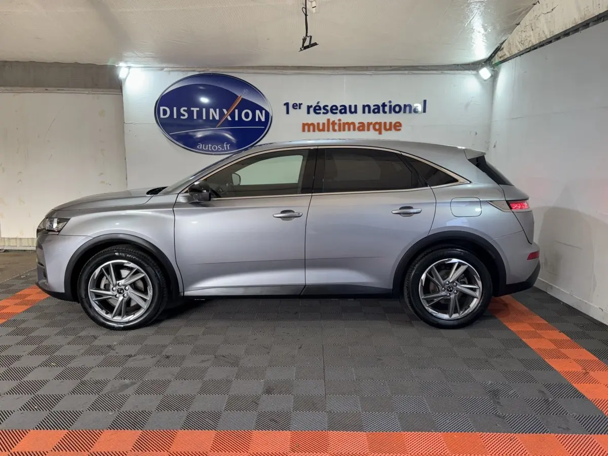 Vue de profil côté gauche d'un DS7 Crossback gris foncé hybride rechargeable garé en intérieur sur sol à damiers noir et orange.