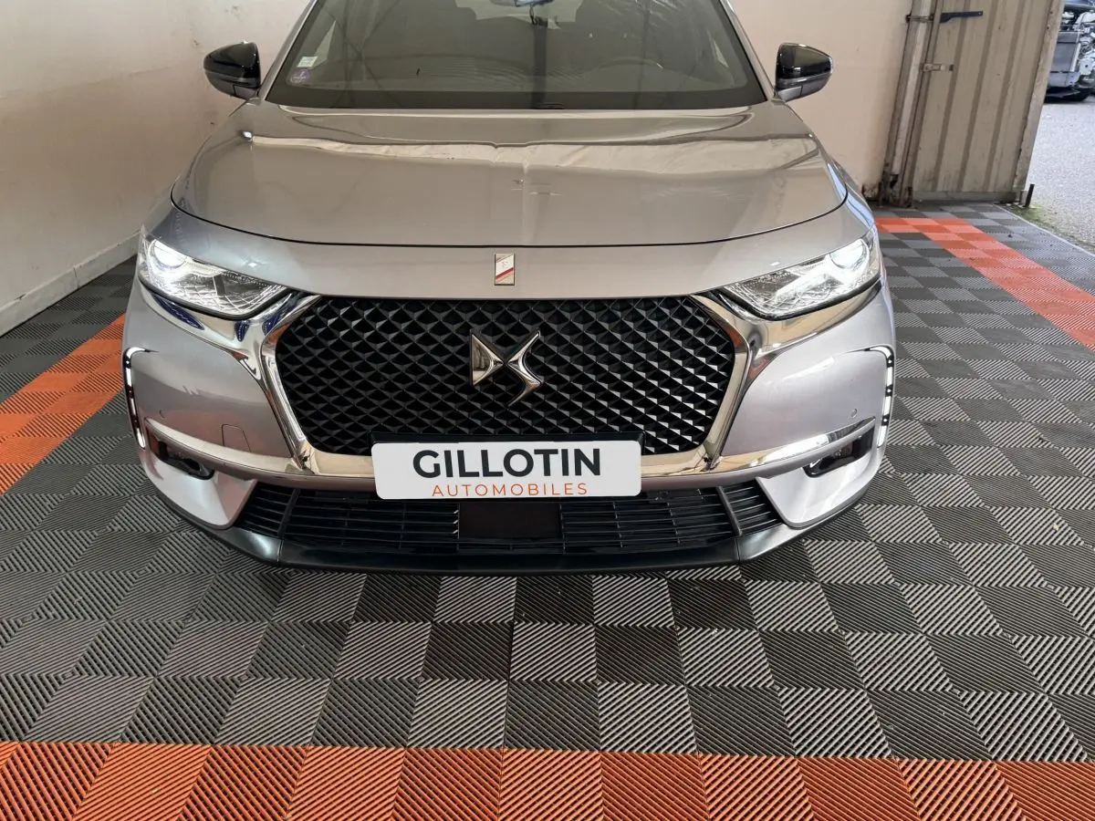 Vue avant d'une DS7 Crossback E-TENSE gris foncé avec calandre noire et phares LED allumés dans un garage.