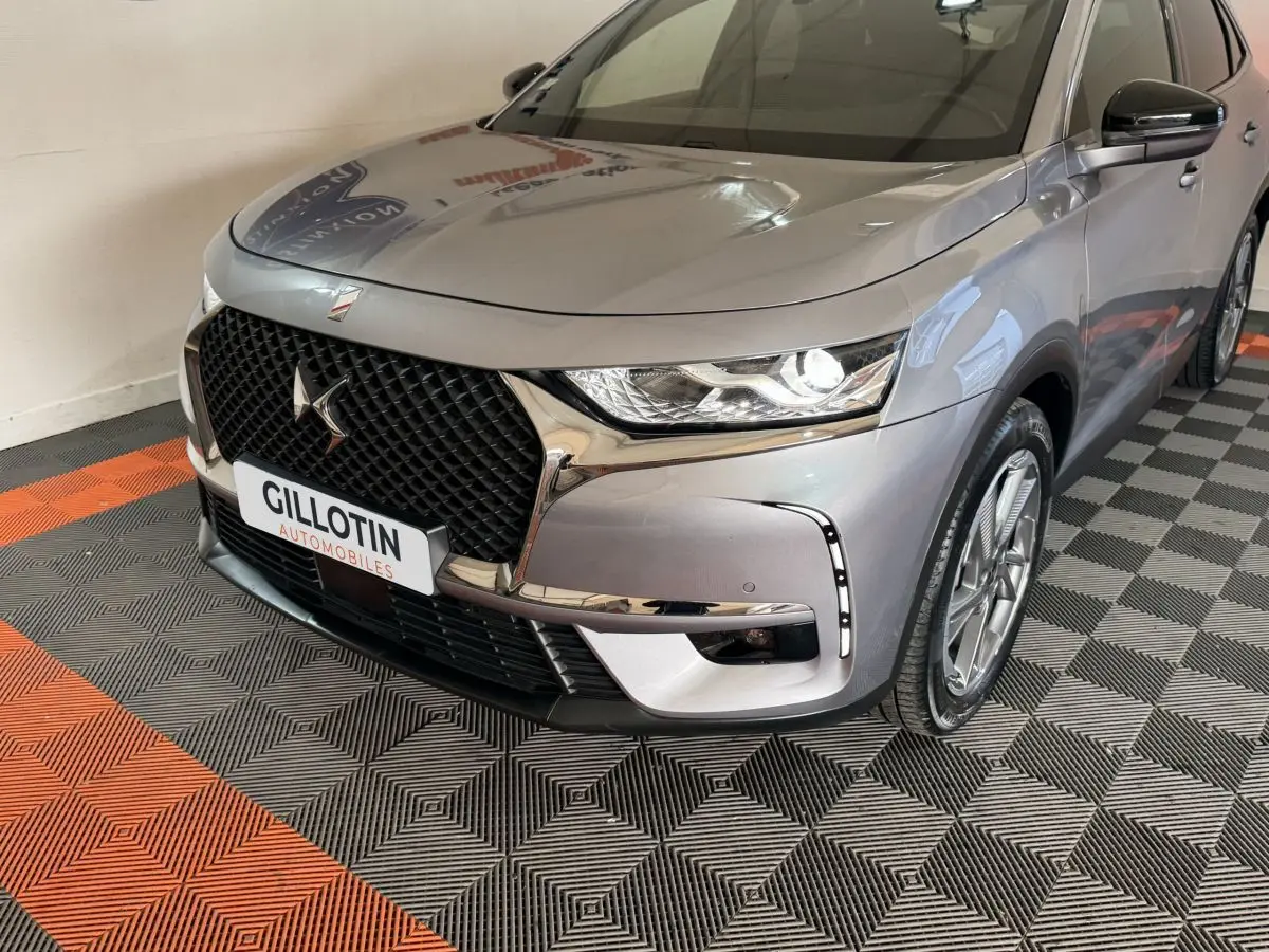 Vue 3/4 avant droit du DS7 Crossback E-TENSE gris foncé avec calandre distinctive et feux LED allumés.