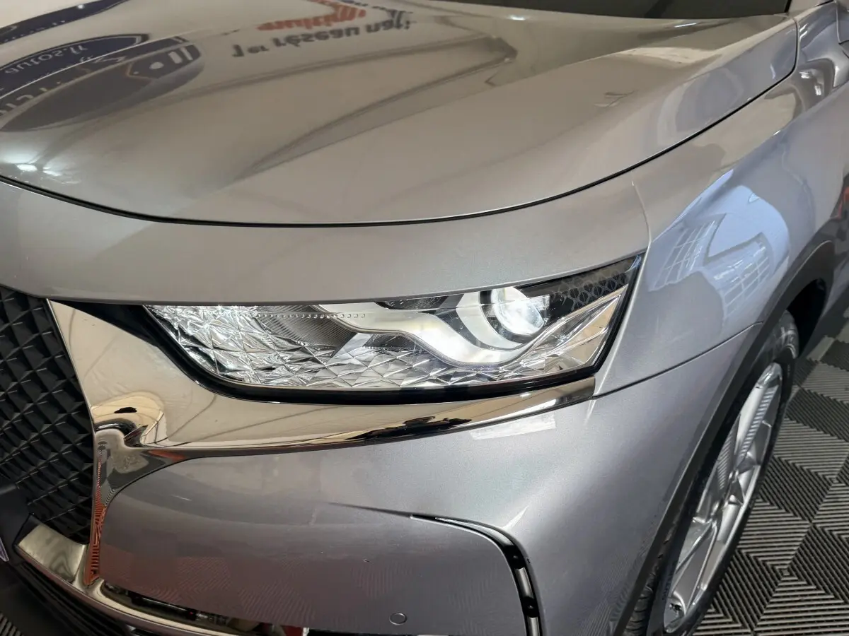 Gros plan sur le phare avant droit gris foncé du DS7 Crossback E-TENSE 225 BASTILLE + avec calandre chromée.