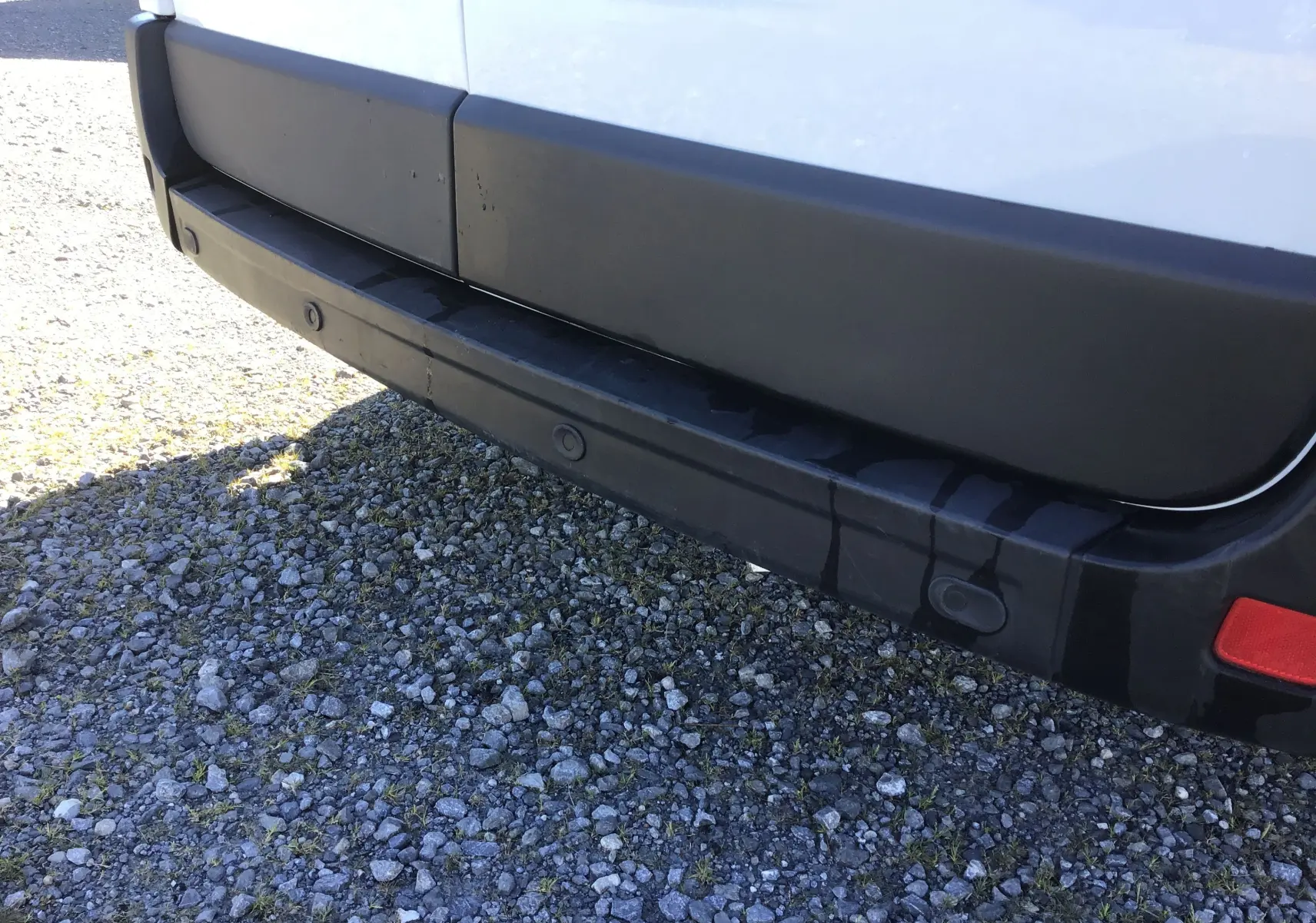 Gros plan sur le pare-chocs arrière noir du Renault Master blanc, montrant les capteurs de recul intégrés.