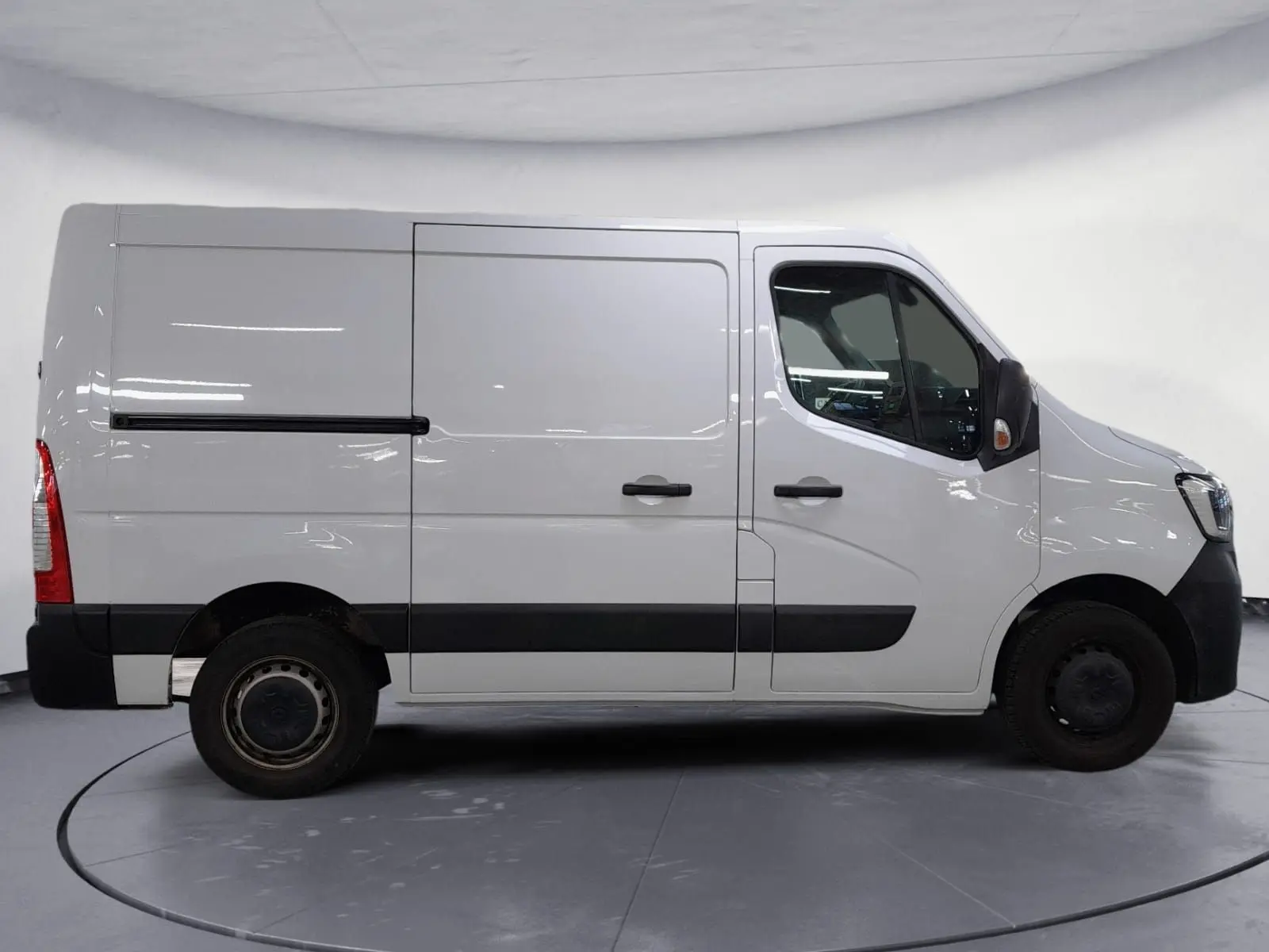 Vue de profil côté gauche d’un utilitaire Renault Master blanc avec bande noire et jantes acier, stationné sur un sol gravillonné.