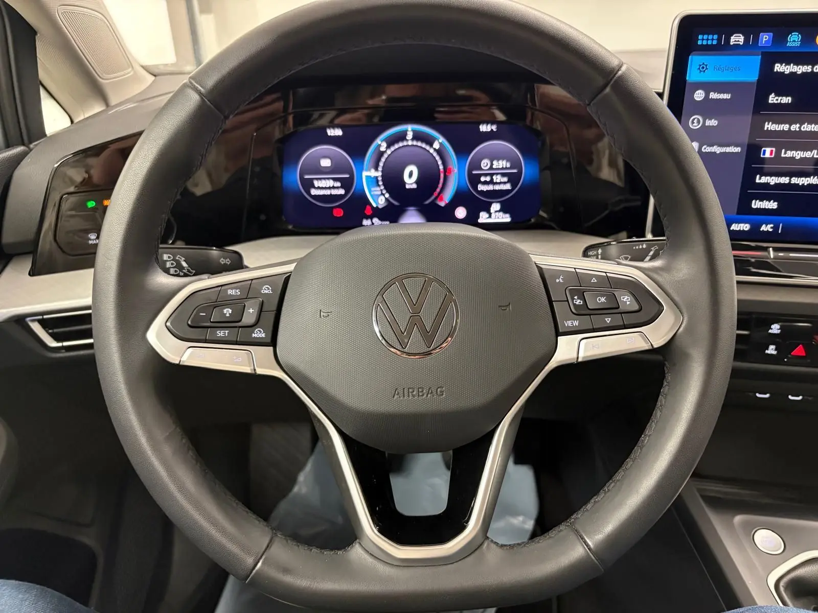 Gros plan sur le volant multifonction noir avec logo Volkswagen, tableau de bord digital et écran tactile du Volkswagen Golf 2025.