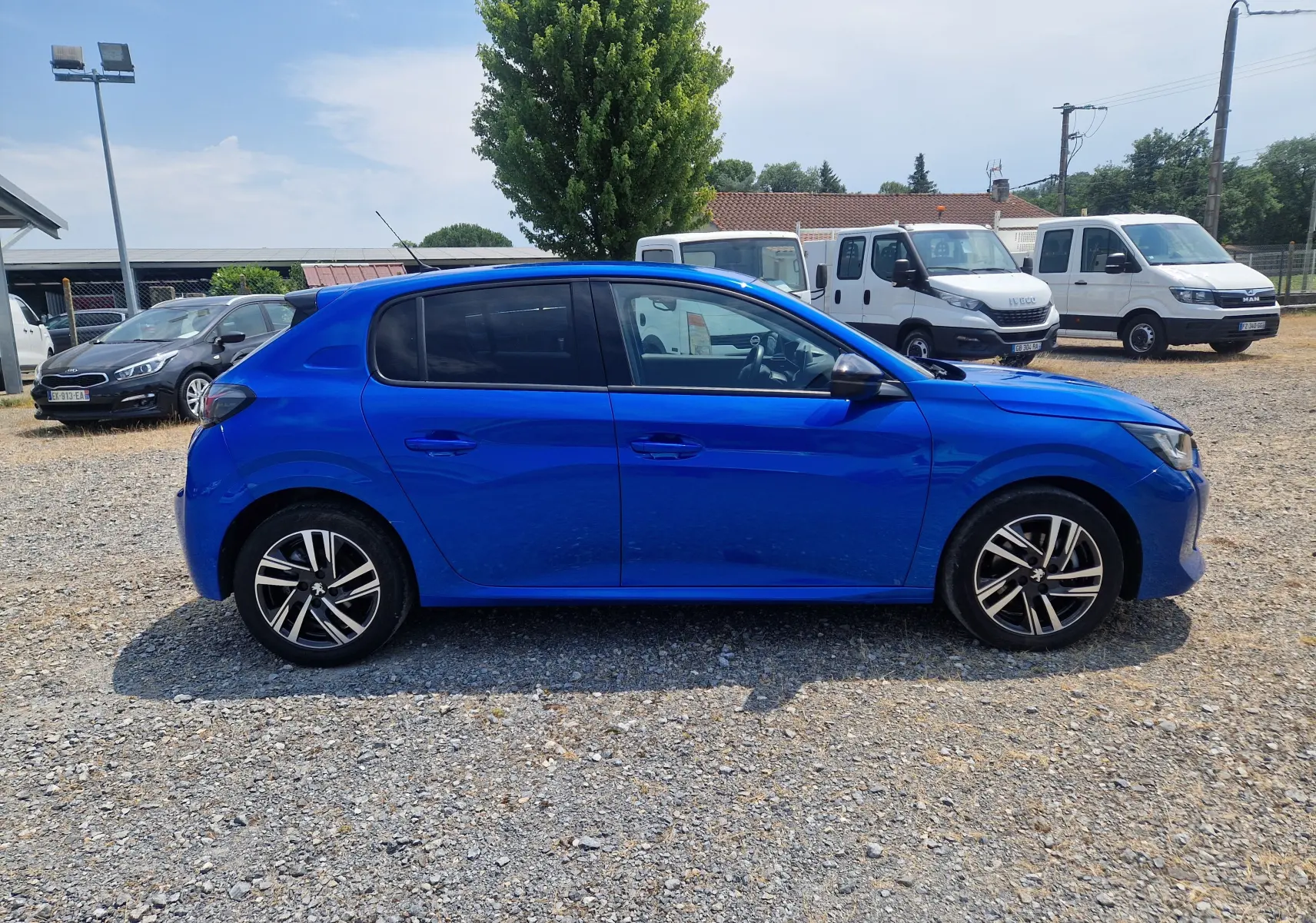 Peugeot 208 bleu Vertigo vue de profil côté gauche sur un sol gravillonné avec jantes alliage noires et argentées.