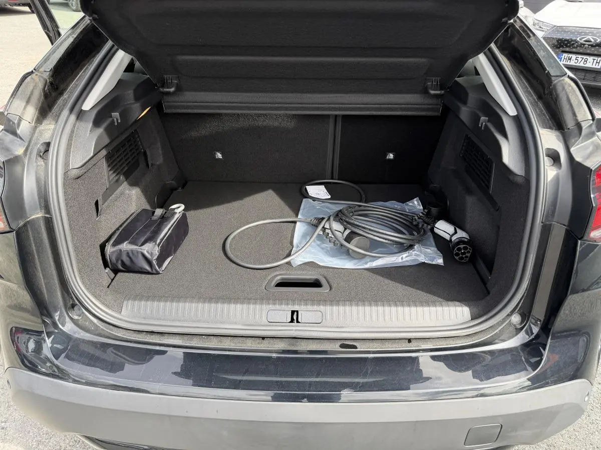 Coffre ouvert de la Citroën C4 ë-136 noir brillant, avec câble de recharge électrique visible à l'intérieur.