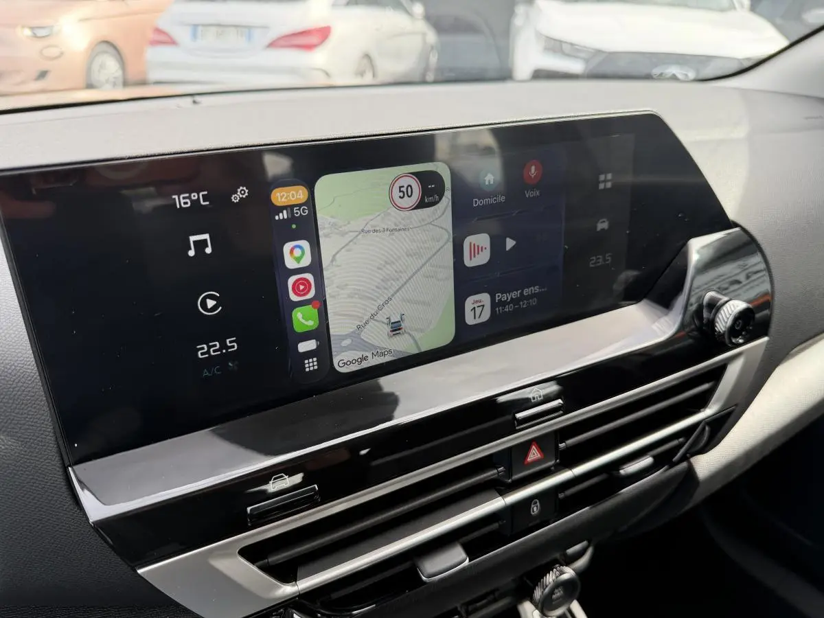 Vue rapprochée de l’écran tactile central du tableau de bord de la Citroën C4 ë-136 noir, affichant la navigation et la climatisation.