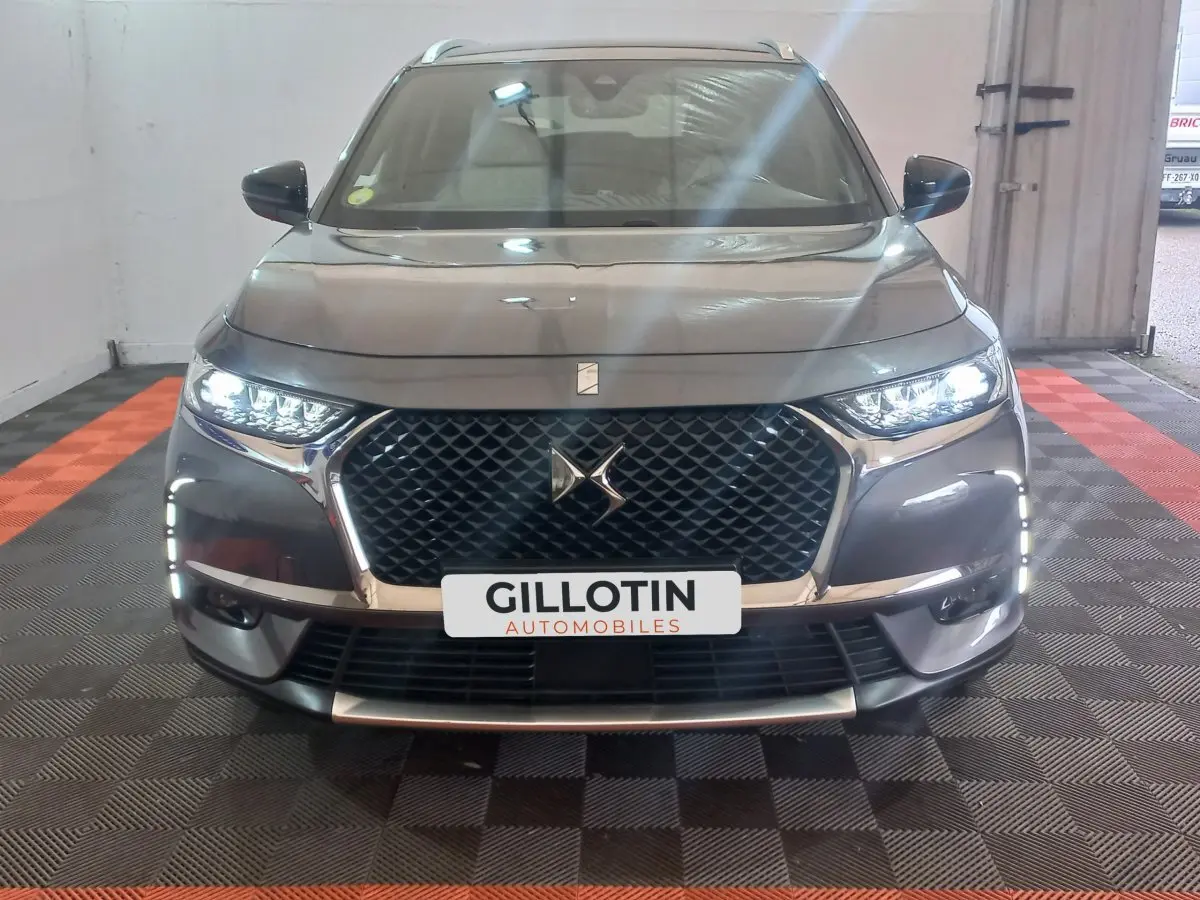 Vue de face du DS7 Crossback gris foncé avec calandre distinctive et feux LED allumés dans un garage.
