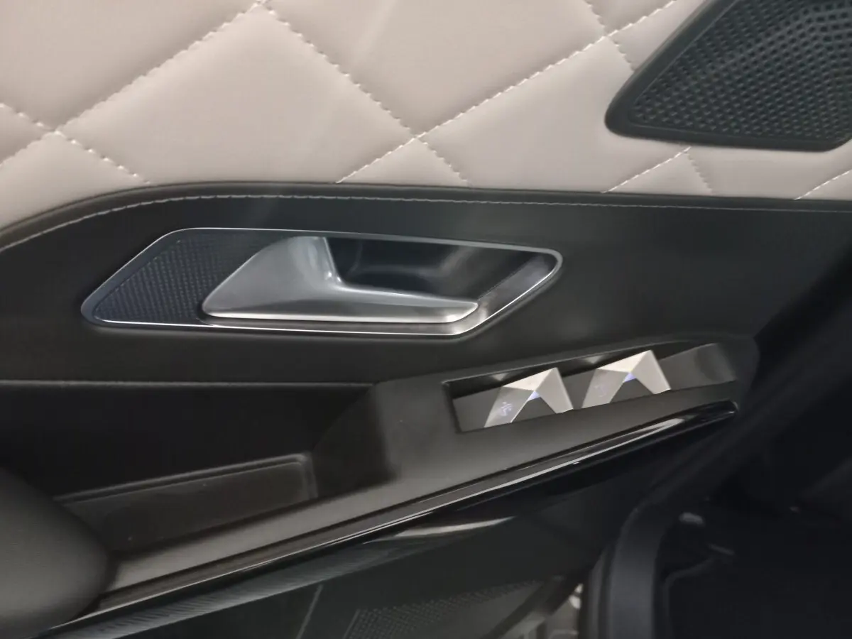 Gros plan sur la poignée intérieure et les commandes de vitre côté gauche du DS7 Crossback gris foncé, finition cuir matelassé.