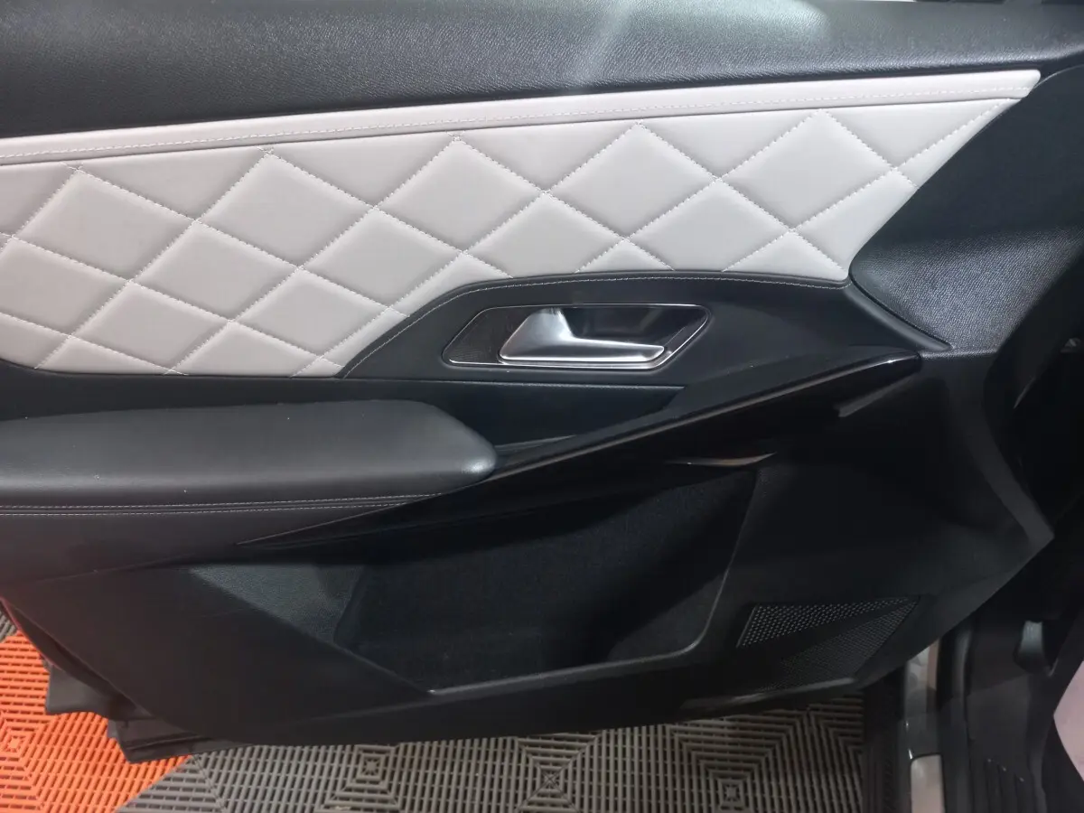 Gros plan sur la porte intérieure côté droit du DS7 Crossback gris foncé, avec cuir matelassé blanc et poignée argentée.
