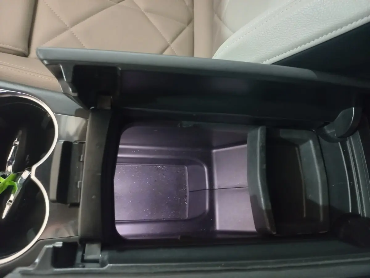 Vue rapprochée de la console centrale ouverte du DS7 Crossback, montrant le rangement intérieur noir et les sièges cuir beige.