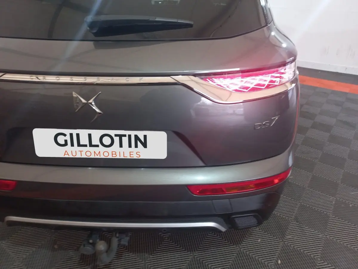 Vue arrière droite du DS7 Crossback gris foncé avec feux LED allumés et attelage visible en garage.