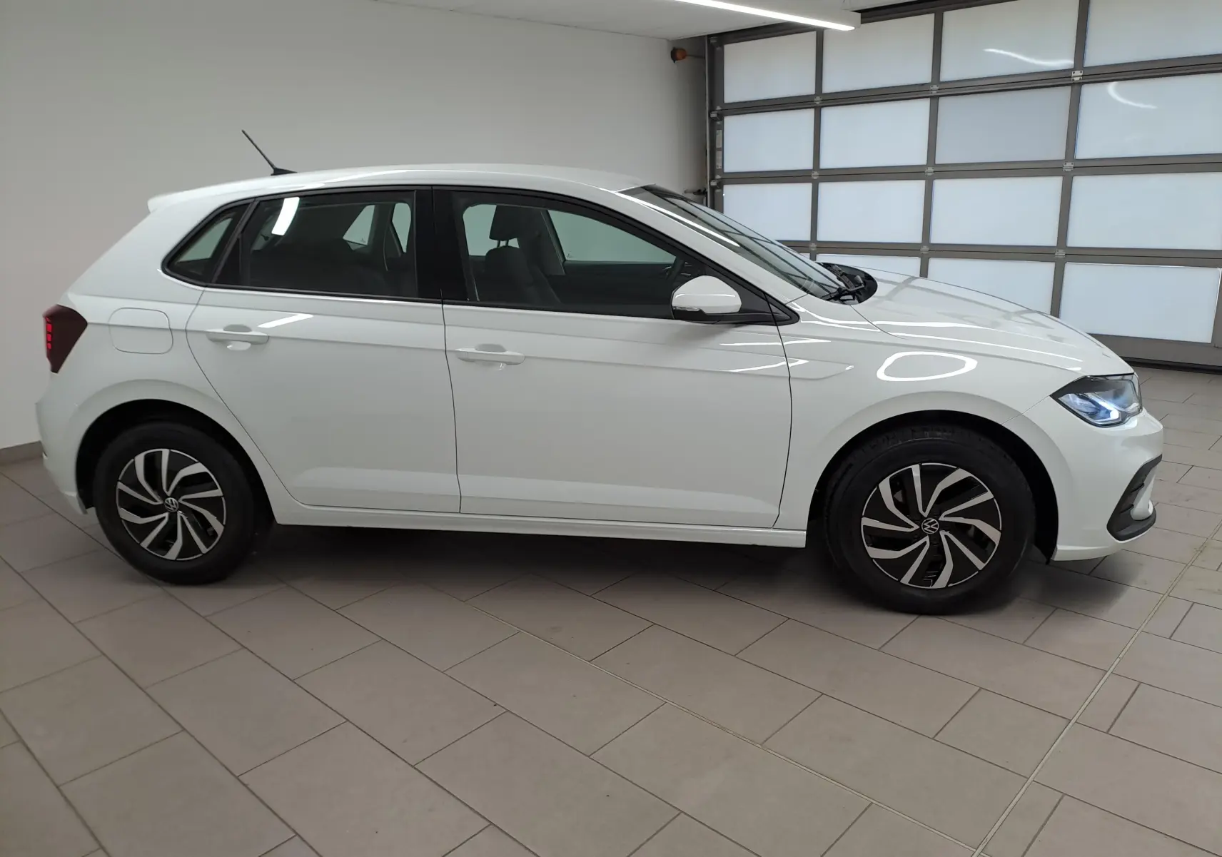 Vue de profil côté gauche d'une Volkswagen Polo blanche 2024 avec jantes au design moderne, stationnée en intérieur.