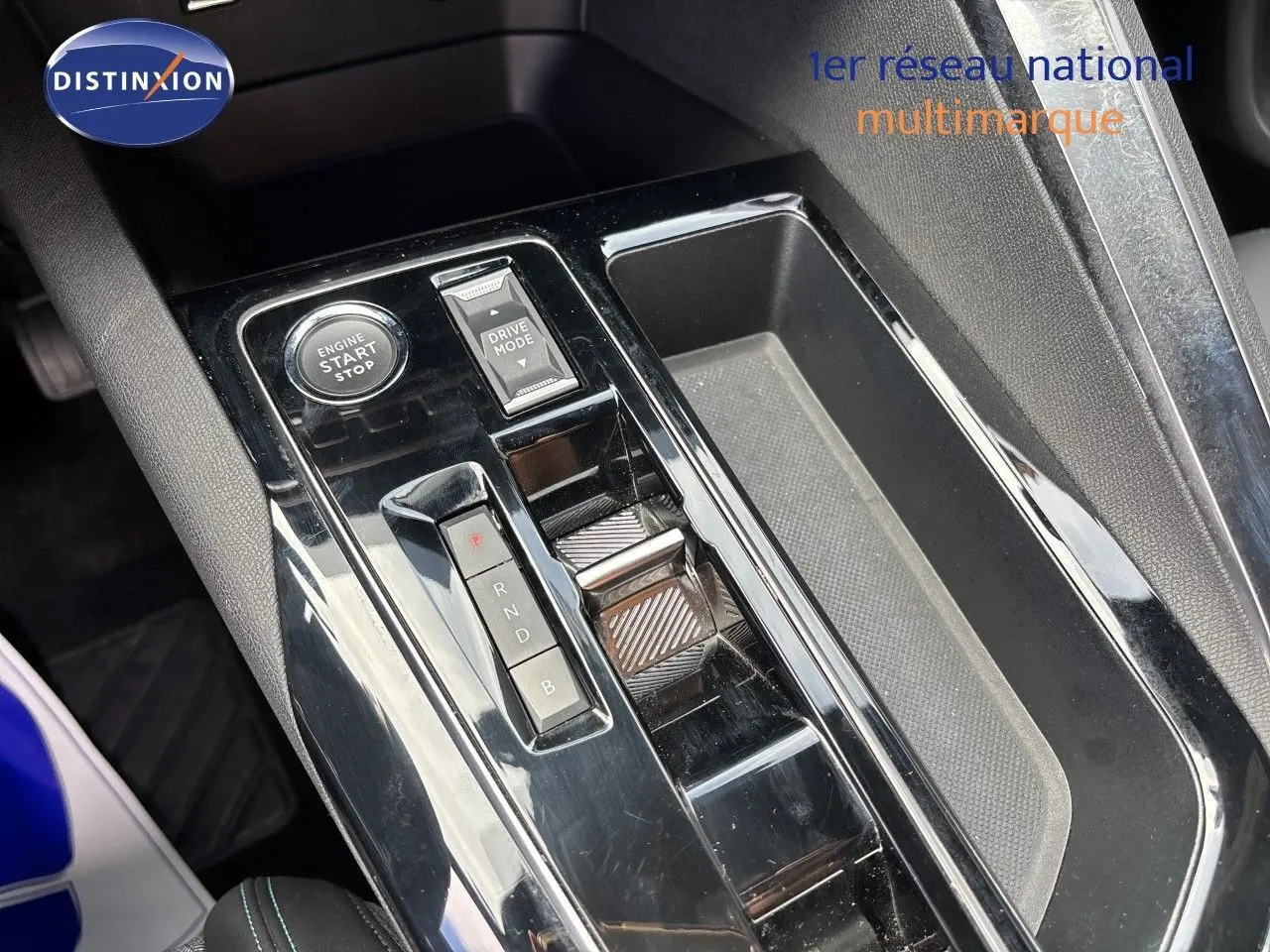 Gros plan sur la console centrale noire brillante du Peugeot 3008 Hybrid 180ch, avec bouton start/stop et sélecteur de mode de conduite.