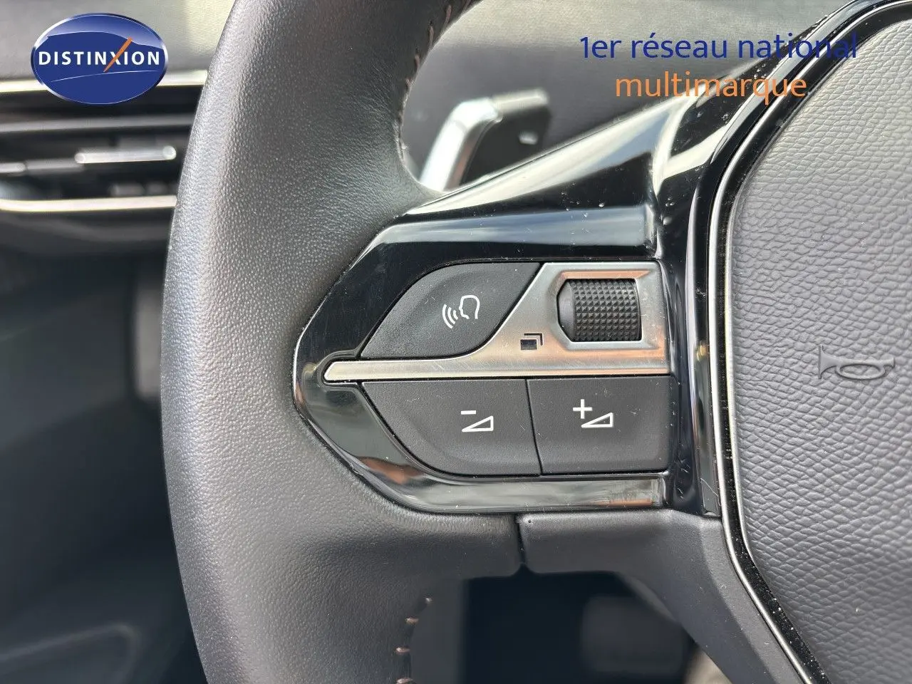 Gros plan sur les commandes gauche du volant noir du Peugeot 3008 Hybrid 180ch 2024, avec boutons de volume et fonction mains libres.