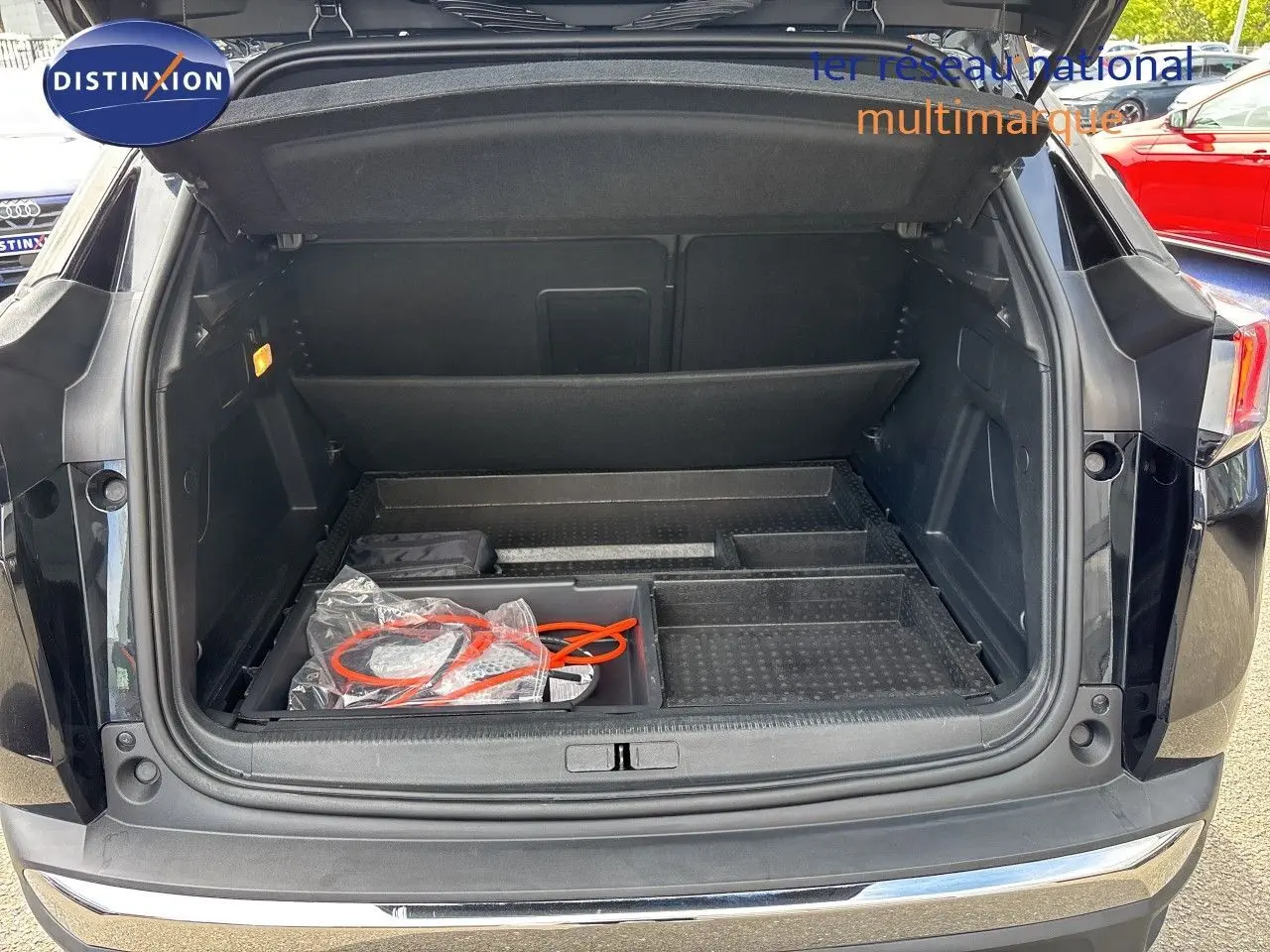 Coffre ouvert vu de l'arrière d'un Peugeot 3008 noir métal 2024 avec câble de recharge visible dans le compartiment.