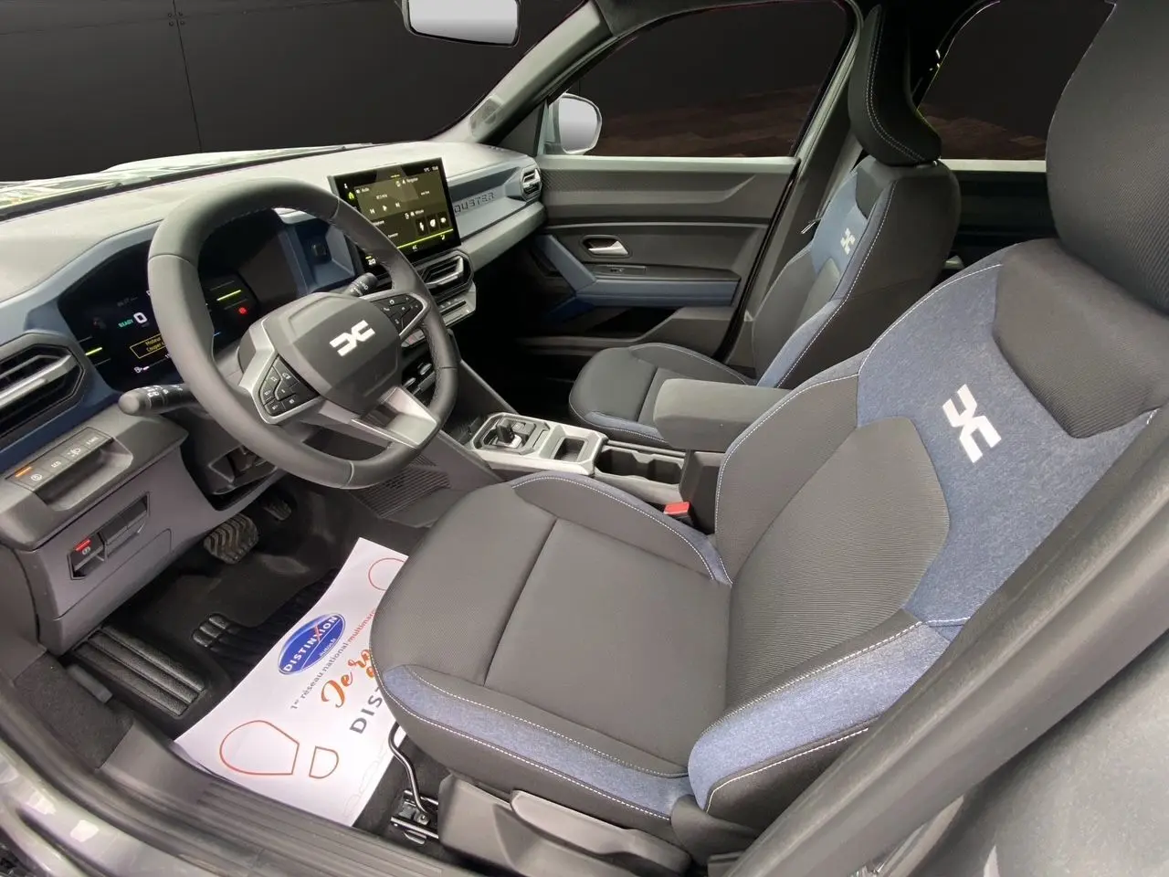 Vue intérieure côté conducteur du Dacia Duster hybride 2025 avec sièges noirs et bleus et tableau de bord numérique.