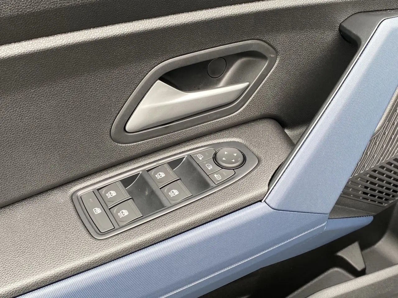 Détail de la porte côté conducteur du Dacia Duster 2025 hybride, avec habillage noir et bleu et commandes de vitres électriques.