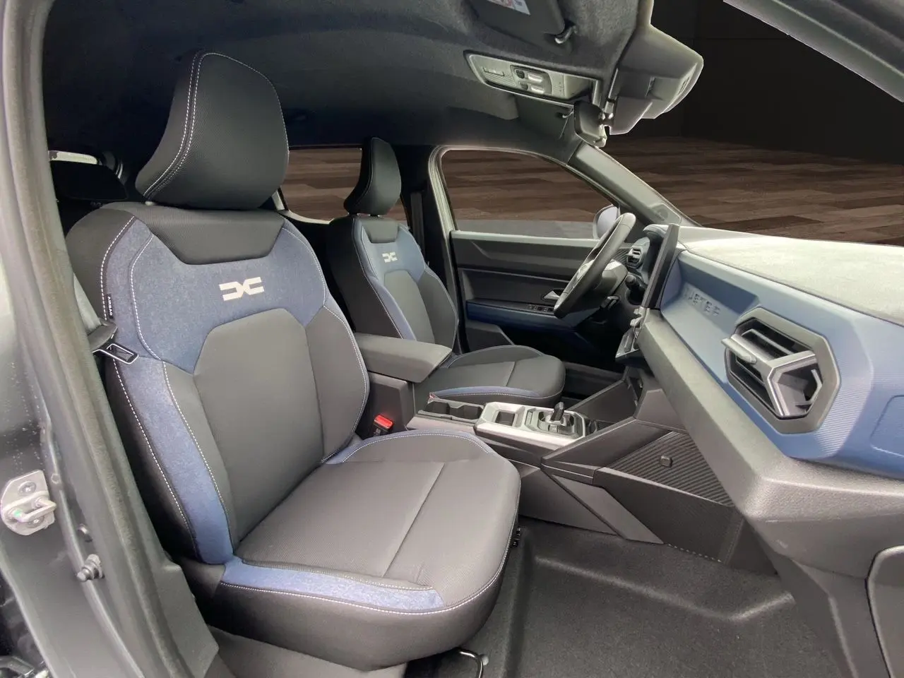 Intérieur du Dacia Duster hybride 2025 montrant les sièges avant bleu et noir et le tableau de bord côté droit.