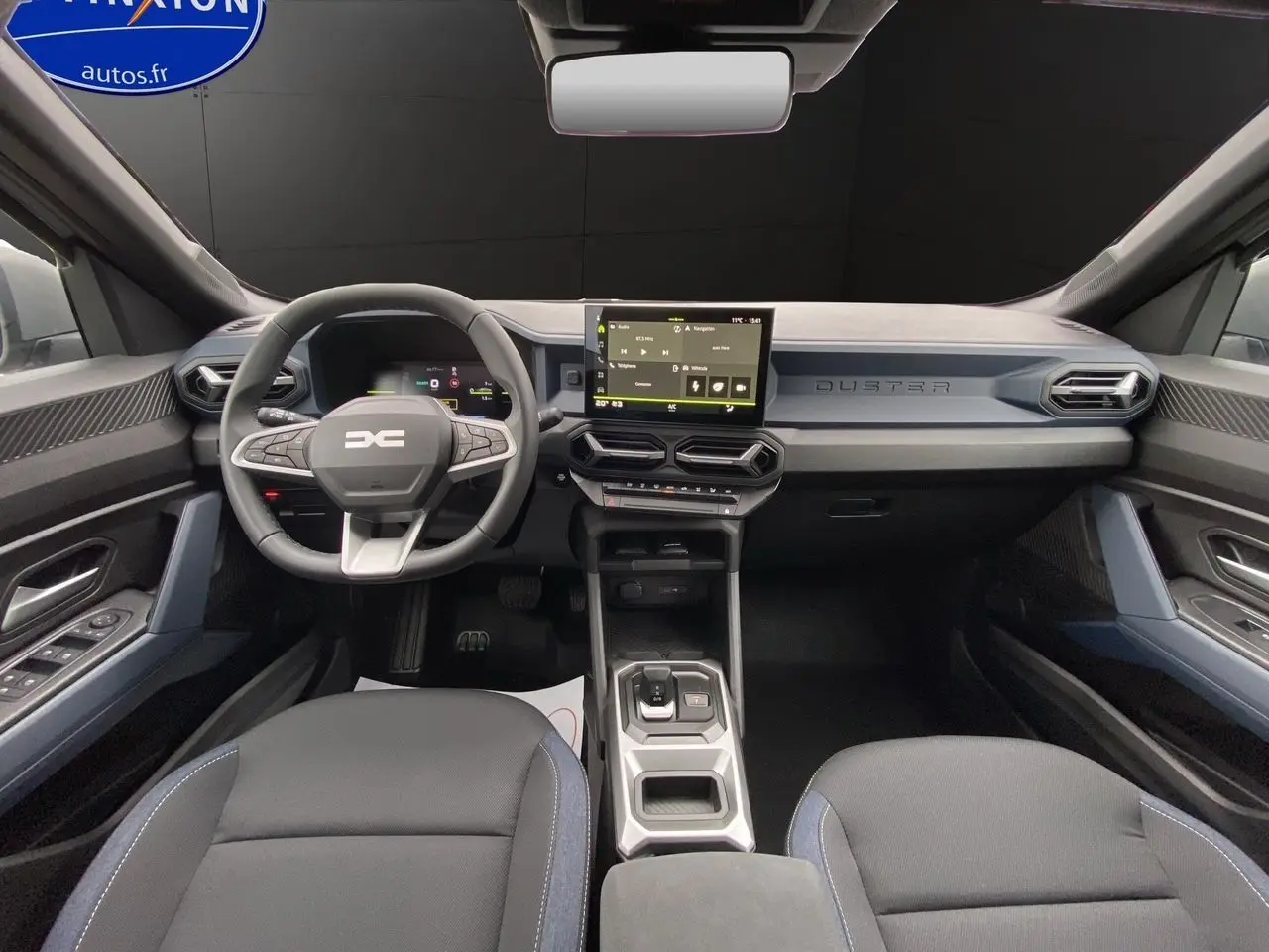 Vue intérieure avant du Dacia Duster 2025, tableau de bord moderne avec écran tactile et volant multifonction noir et bleu.