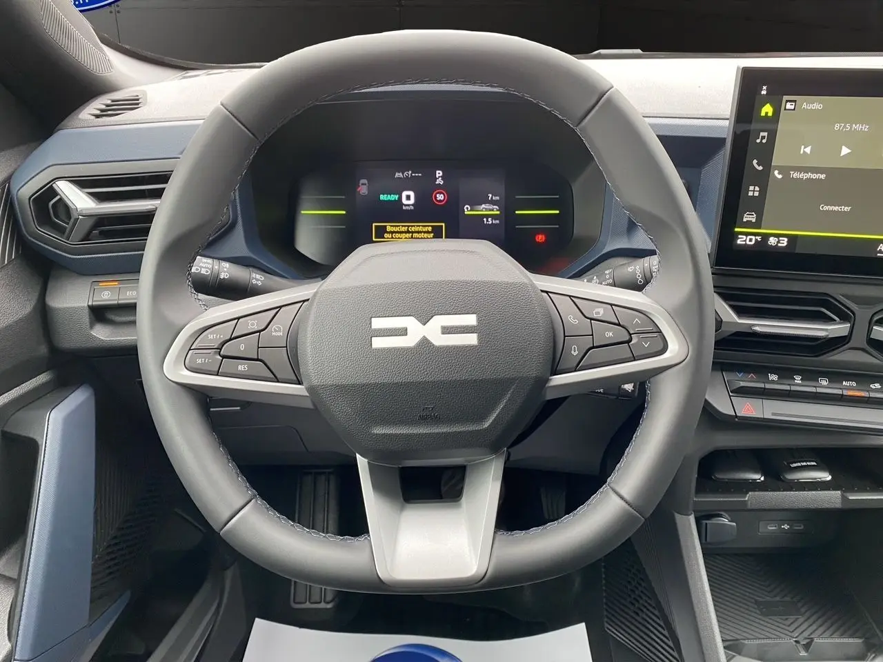 Vue rapprochée du volant et tableau de bord numérique du Dacia Duster hybride 2025 avec écran tactile et commandes intégrées.