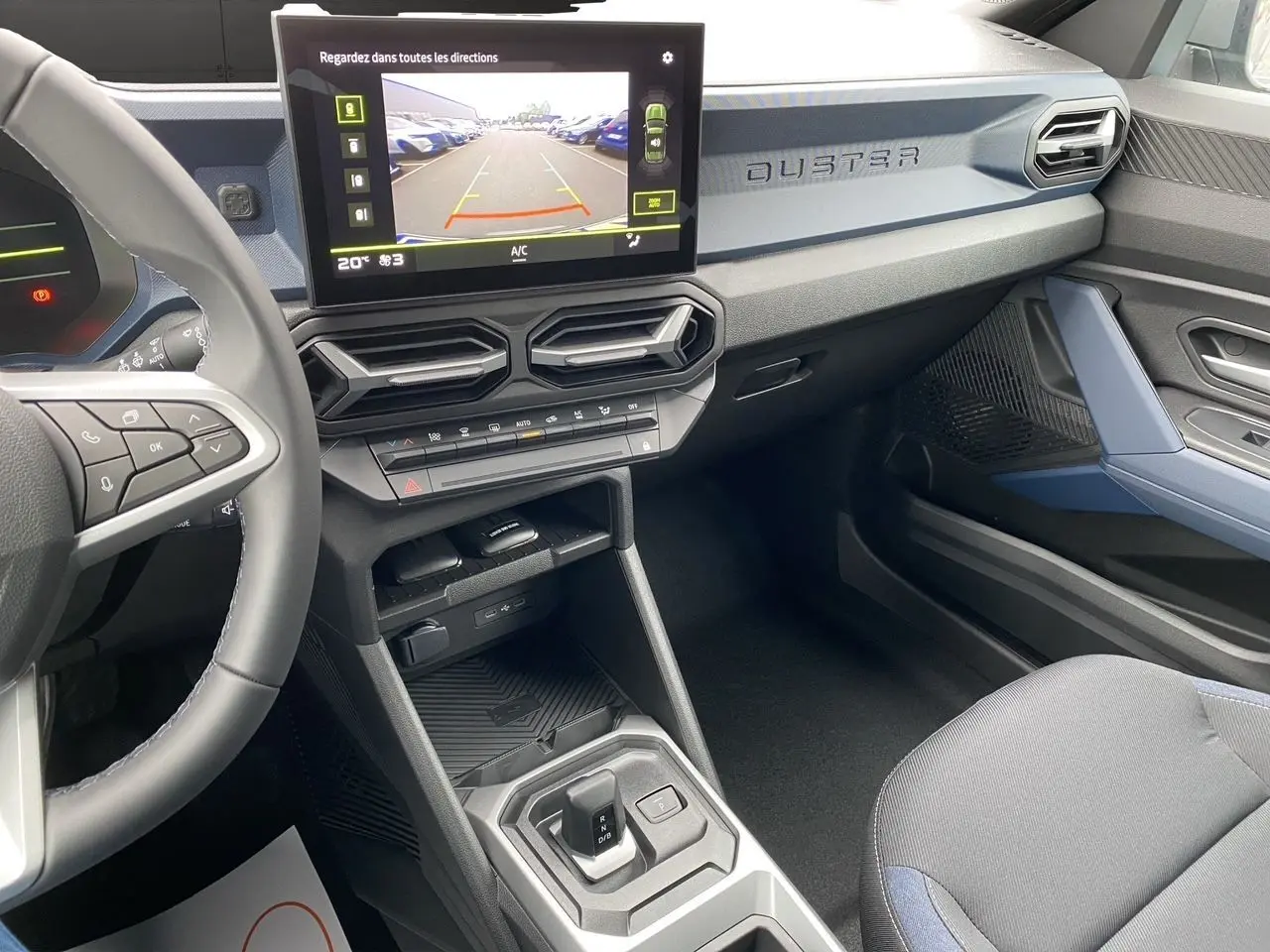 Vue intérieure côté passager du tableau de bord gris bleu du Dacia Duster hybride 2025 avec écran multimédia et volant noir.