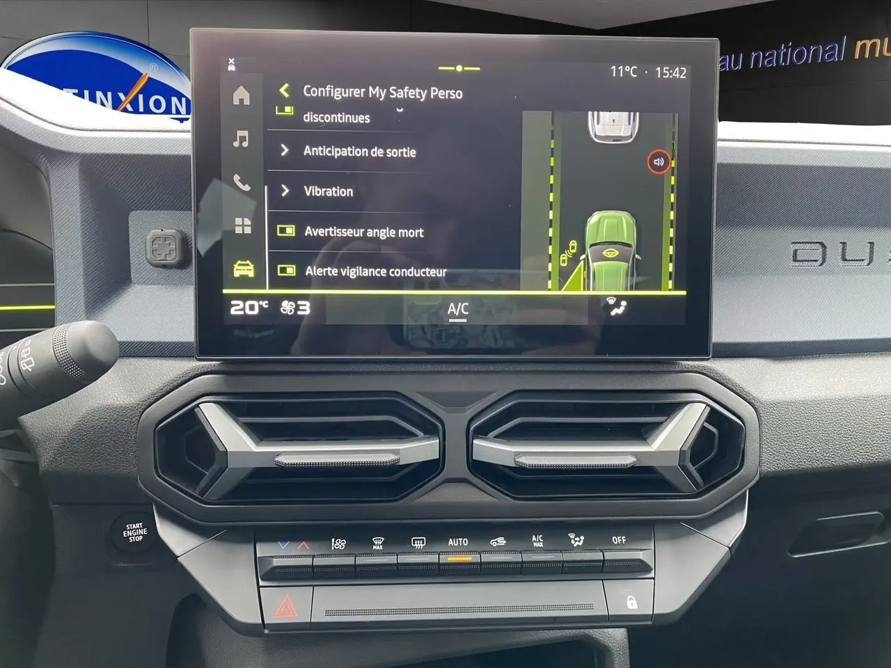 Tableau de bord noir-bleu du Dacia Duster 2025 avec écran tactile affichant les aides à la conduite et aérateurs hexagonaux.