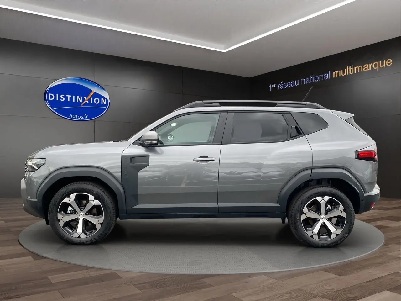Profil droit du Dacia Duster 2025 gris schiste hybride avec jantes alliage et barres de toit noires.