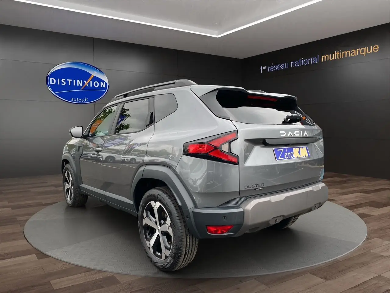 Vue 3/4 arrière droite du Dacia Duster hybride gris schiste avec jantes alliage et feux arrière LED dans un showroom.