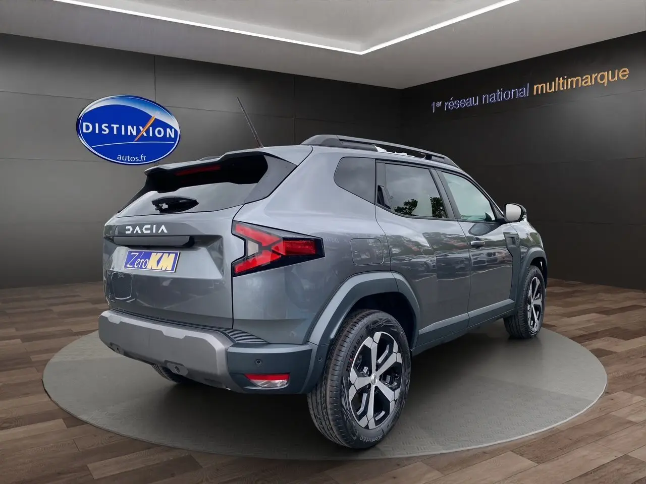 Vue 3/4 arrière droite du Dacia Duster hybride 2025 en gris schiste avec jantes alliage et barres de toit noires.