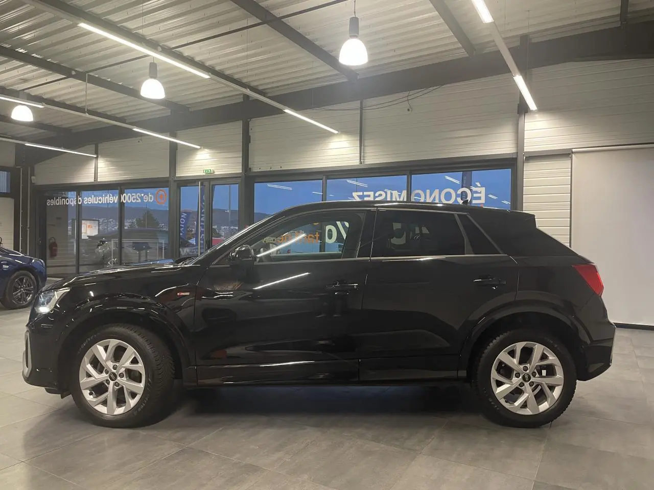 Vue de profil côté gauche d'un Audi Q2 noir métallisé S line avec jantes alliage en showroom.