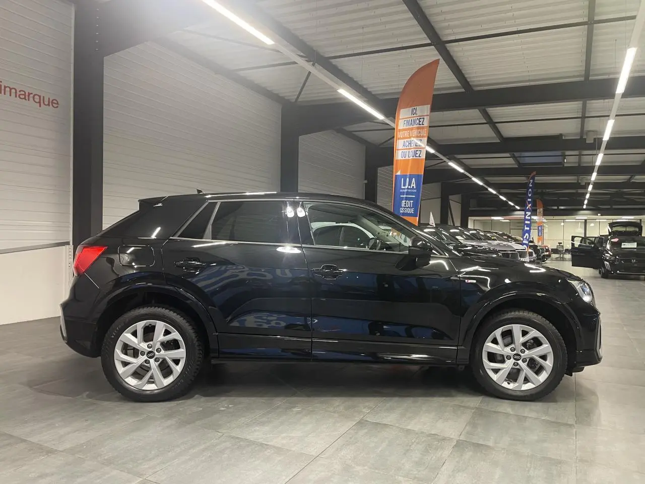 Audi Q2 noir métallisé vue de profil côté gauche dans un showroom avec jantes alliage et vitres surteintées.