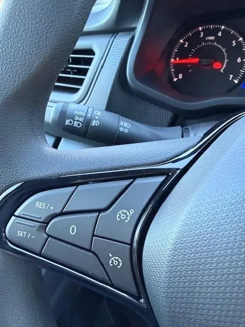 Gros plan sur les commandes du volant multifonctions du Renault Trafic Fourgon gris clair, avec régulateur de vitesse visible.