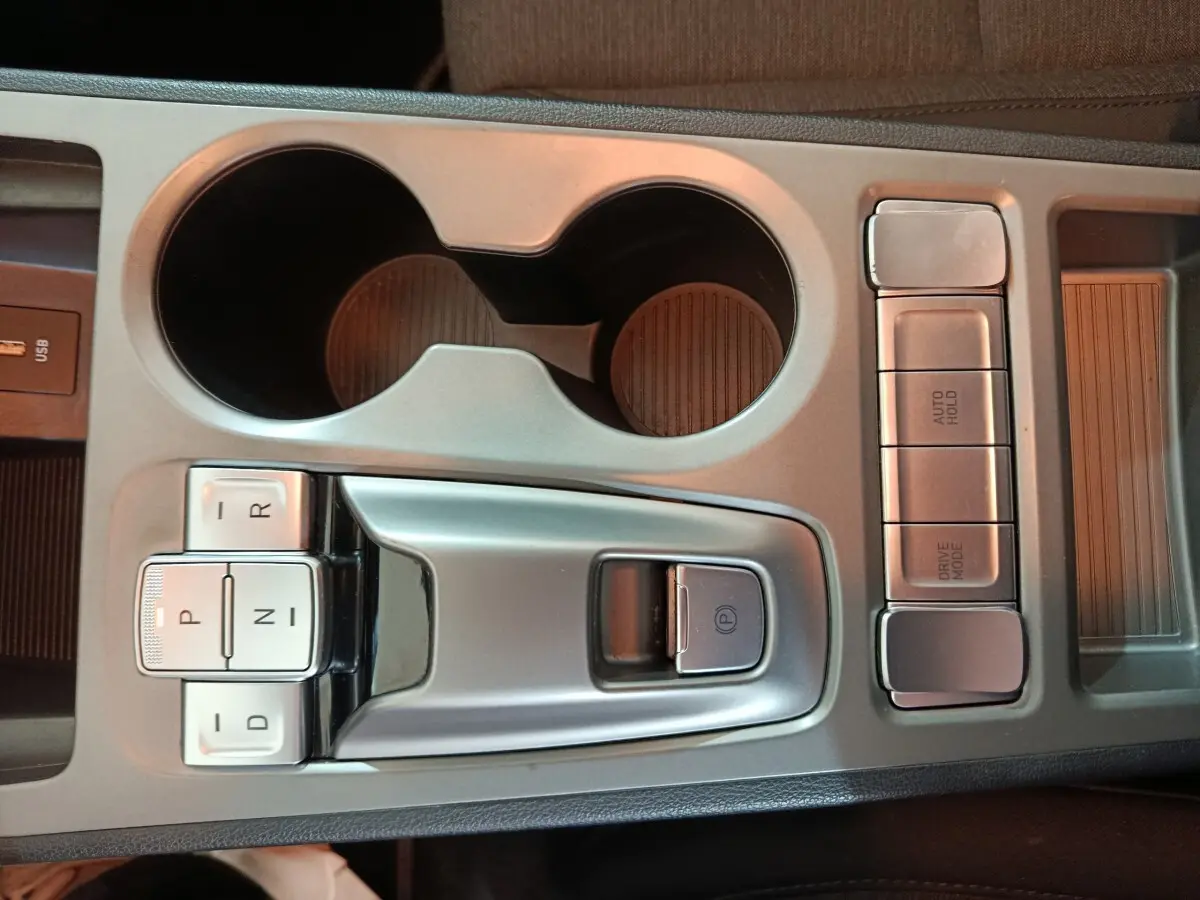 Vue rapprochée de la console centrale grise avec commandes de boîte auto et porte-gobelets du Hyundai Kona électrique bleu 2022.