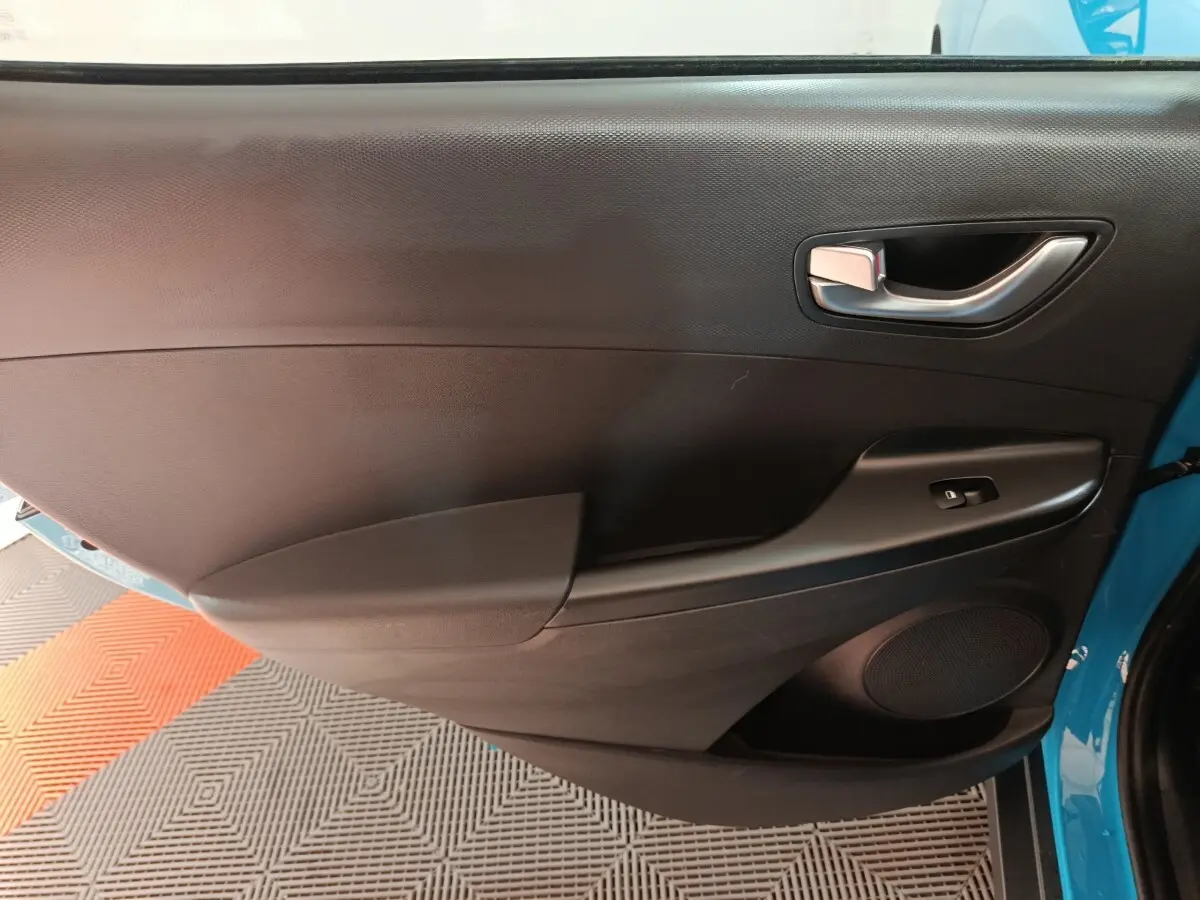 Vue rapprochée de la porte avant gauche noire avec poignée argentée du Hyundai Kona bleu électrique 2022.
